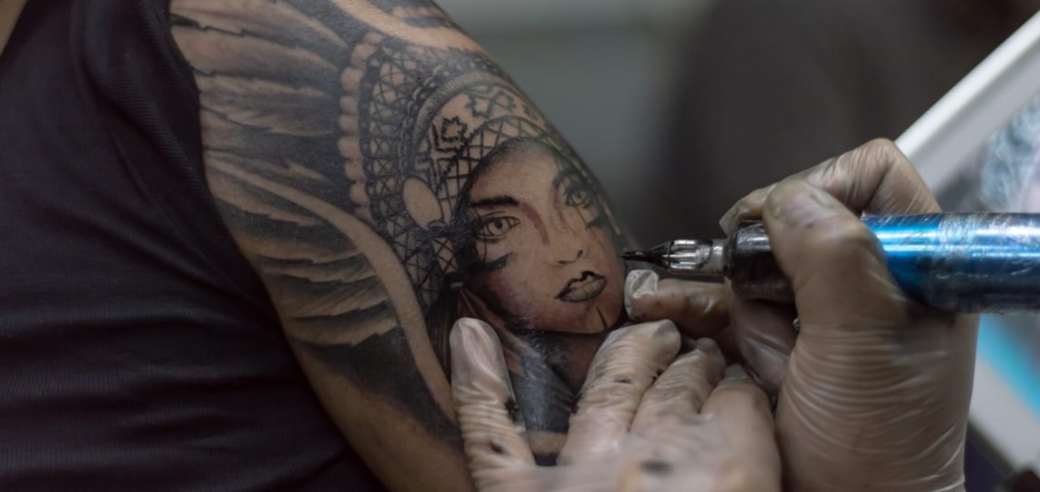 A closeup shot tattoo artist holding a tattoo machine tattooing a person