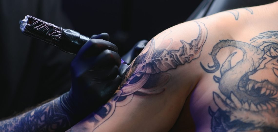 Tattoo artist hands wearing gloves and holding a tattoo machine.