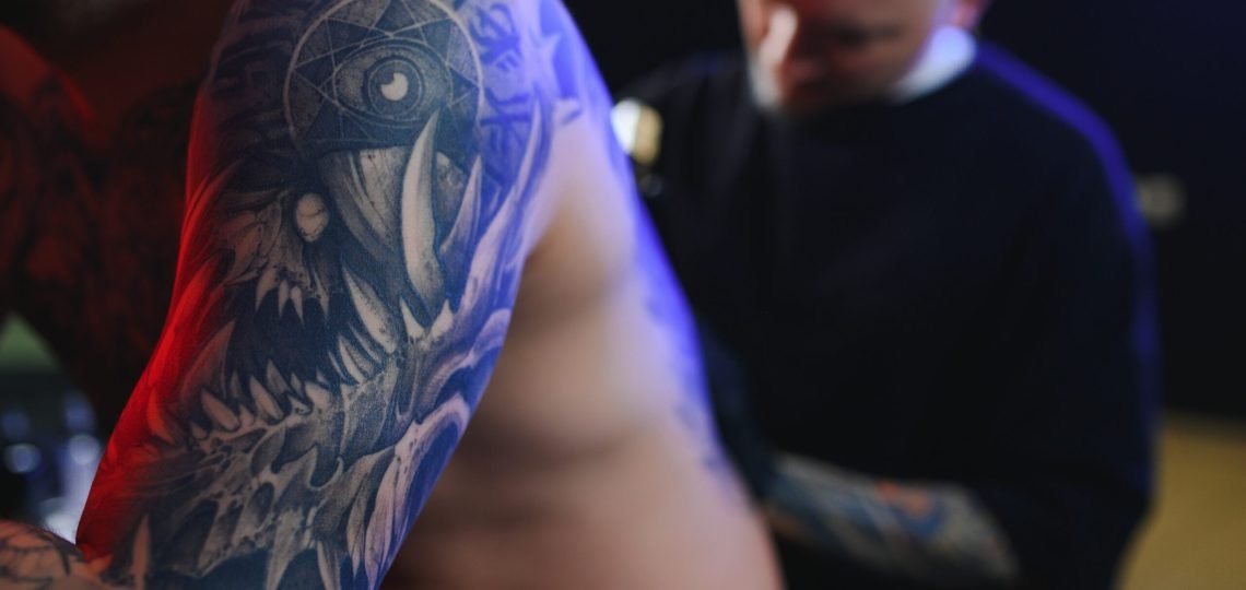 Tattooing. Man creating a picture on his back by a professional tattoo artist.