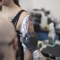 Tattooist removing tattoo stencil from woman's arm