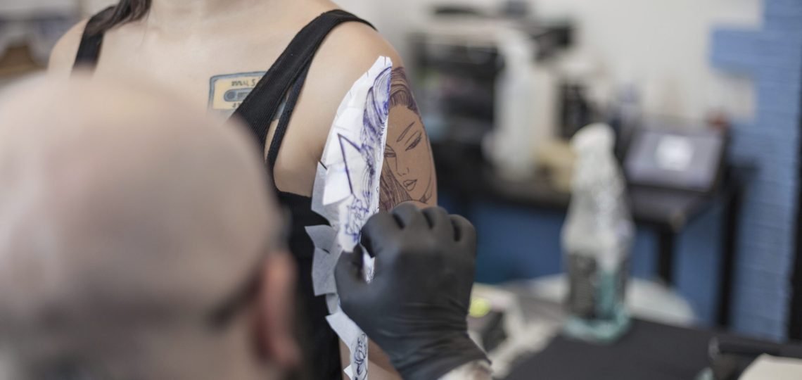 Tattooist removing tattoo stencil from woman's arm