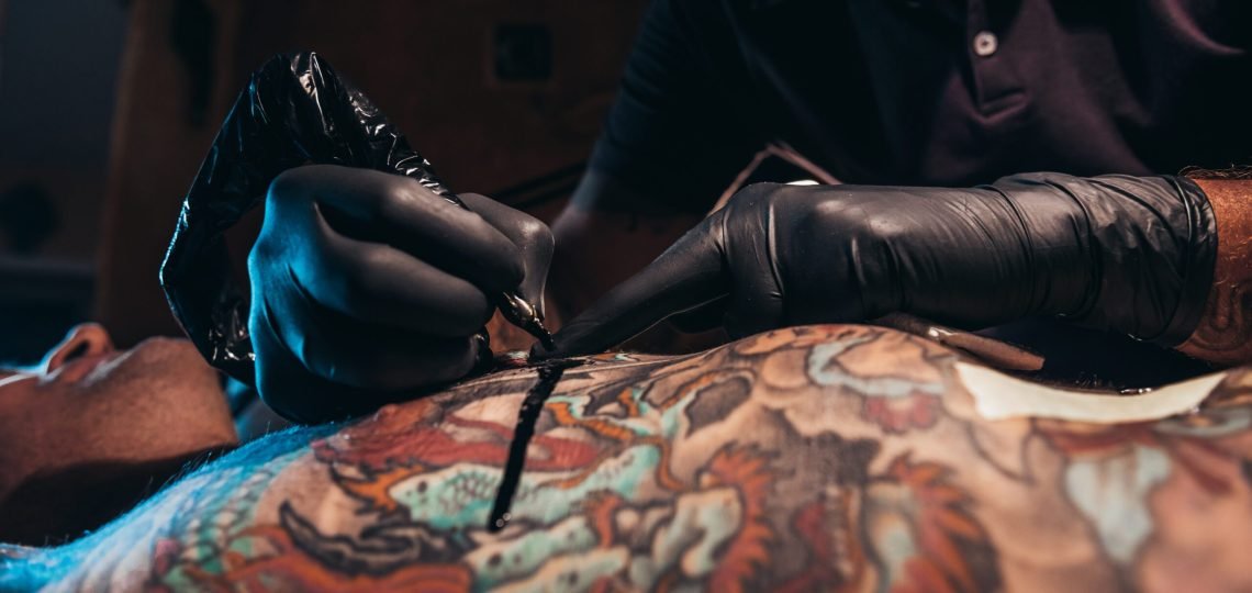 Cropped shot of an artist hands in a protective gloves holding ma machine while the ink is dropping